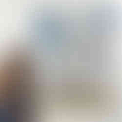 A woman stands beside a large abstract painting featuring soft blue, grey, and white tones with organic shapes