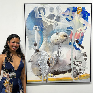 A woman stands beside a large abstract painting featuring soft blue, grey, and white tones with organic shapes
