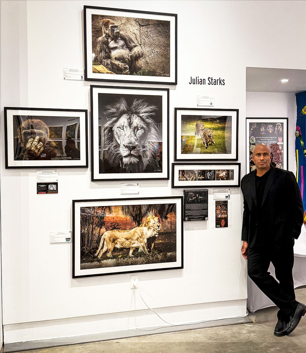 Julian Starks stands beside a gallery wall of framed wildlife photos, with Julian Starks on the wall.