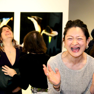 Performer laughing expressively in front of dark floral artworks during Clio Art Fair