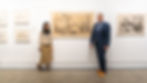 Artist Denny Theocharakis and gallery founder Alessandro Berni posing in front of a large factory-inspired drawing, surrounded by additional framed artworks on a white gallery wall