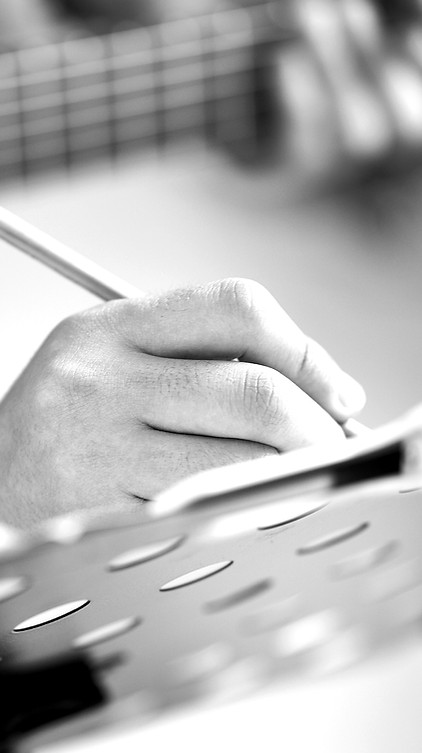Hand writing lyrics on a notebook beside a guitar - creative songwriting process at minardi STUDIO.