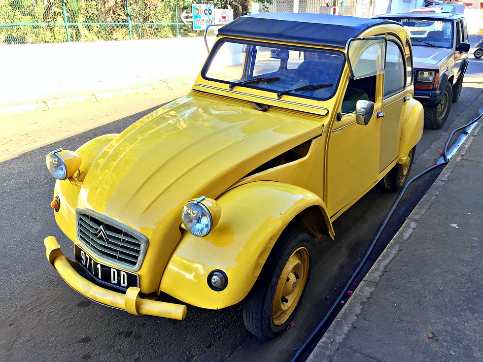 Vintage model car with rounded hub caps, hood, and body. Car is bright yellow with chrome headlights