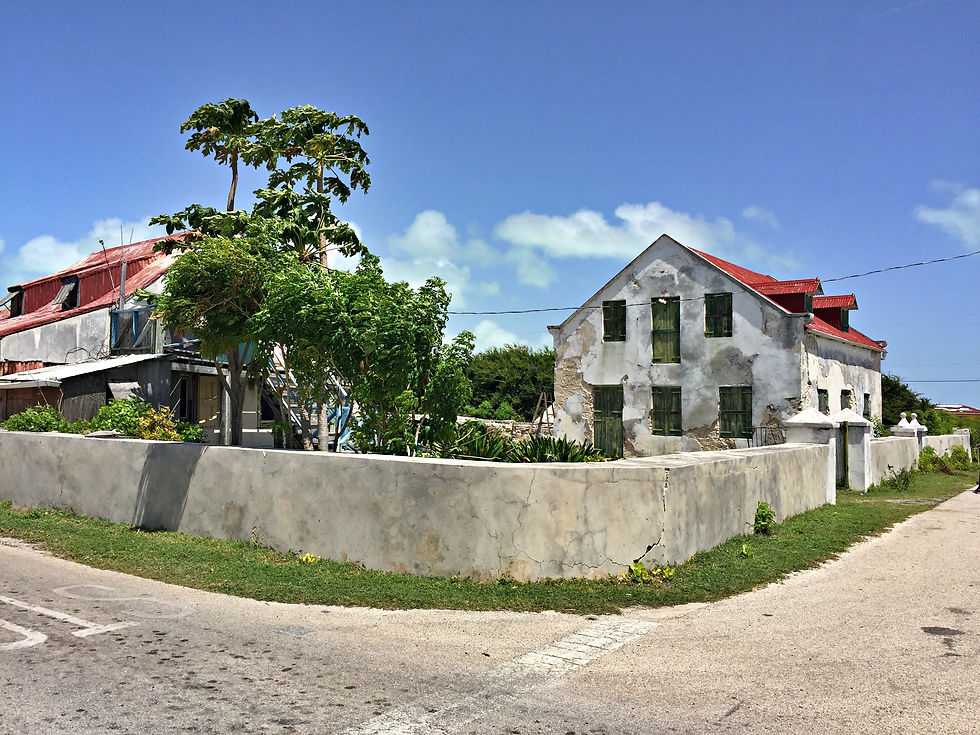Low retaining wall on a street corner, in front of two buildings with peeling white paint and red ro