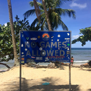 Large, dark blue sign on a white sandy beach reads "No Games Allowed By Order of Management". 