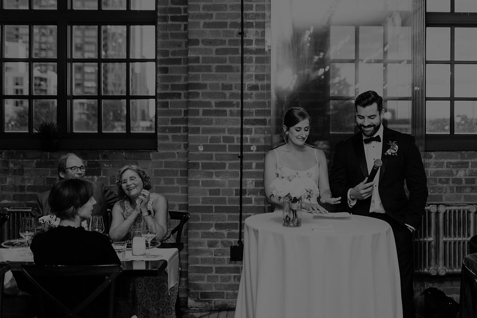 bride and groom speaking to crow with microphone in front of beautiful brick wall