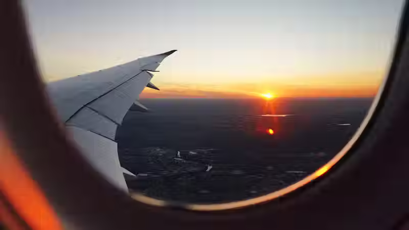 Airplane window showing airplane wing and flight over city during sunrise