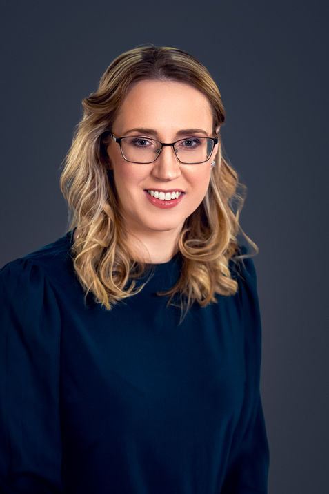 Female executive in glasses and a formal blue outfit, looking approachable in her corporate headshot