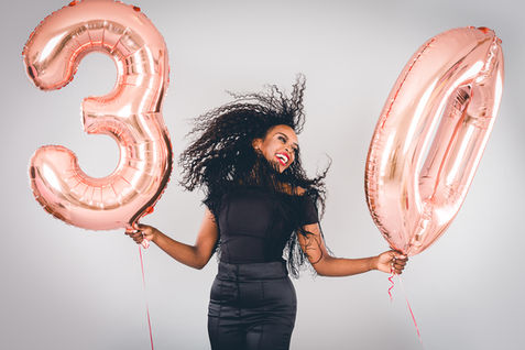 Confident woman posing with large rose gold balloons celebrating her milestone during a studio makeover session.