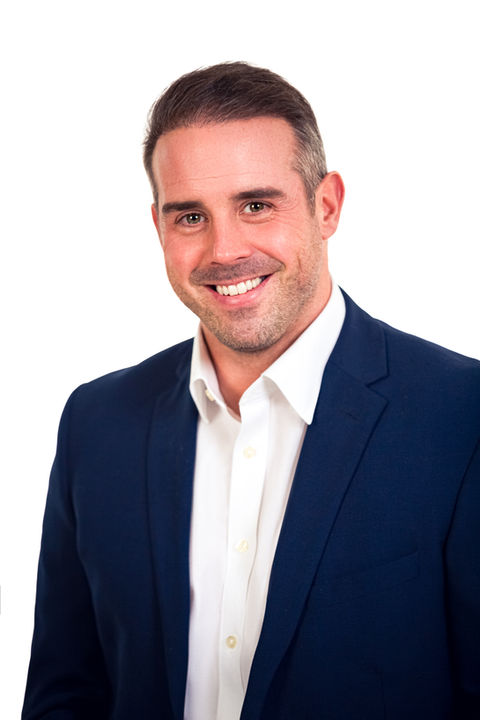 Smiling businessman in a navy suit and white shirt, exuding professionalism in his corporate portrait
