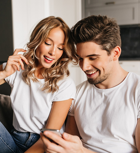 happy-couple-with-smart-phone-looking-screen-smiling-home-portrait-two-young-people-enjoyi