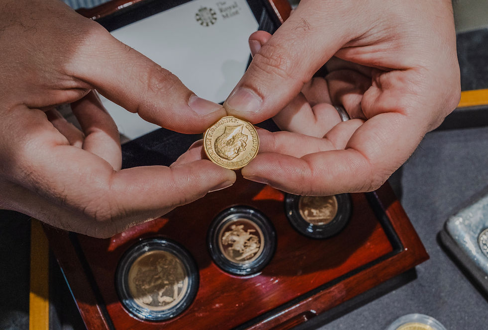 Hands holding a Victorian gold sovereign above a coin tray, with a proof sovereign set and Royal Mint coin set visible in the background.