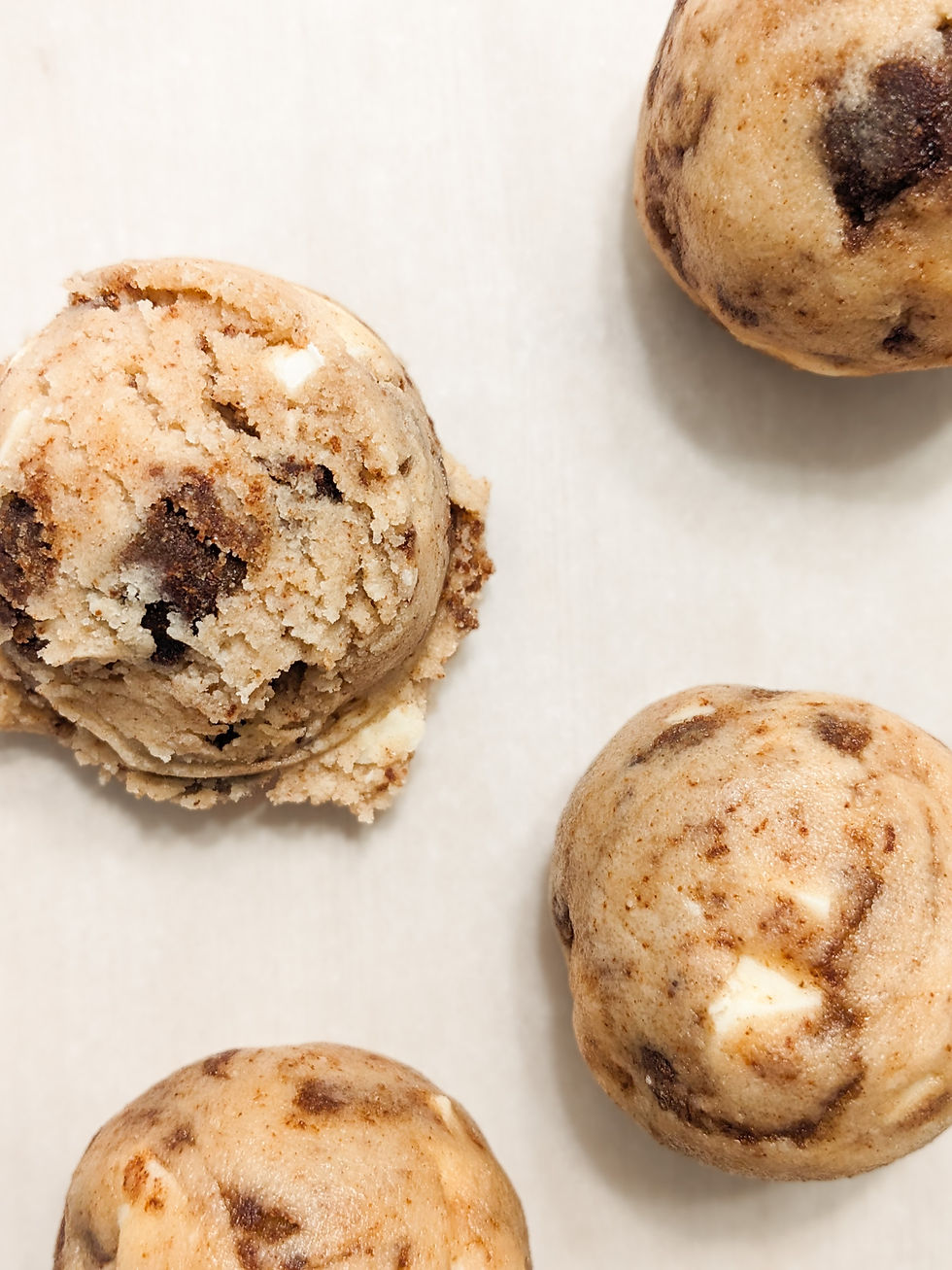 Raw Cinnamon Bun Cookie dough balls studded with white chocolate chunks and cinnamon brown sugar pieces, ready to bake on a parchment-lined tray.