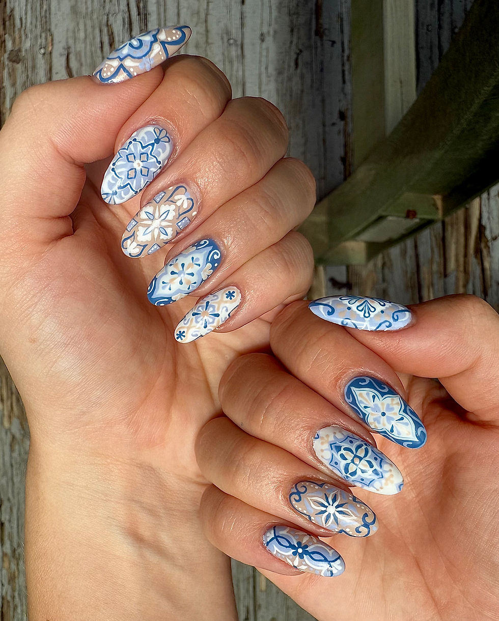Close-up of two hands showing long almond nails with blue-and-white floral tile nail art against a rustic wood background.