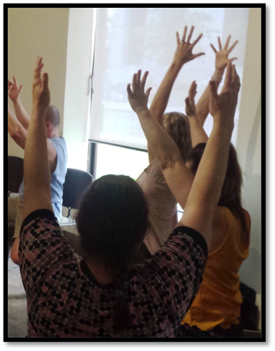 Chair yoga - a group of 4 people sitting in a circle doing chair yoga, their arms stretched up
