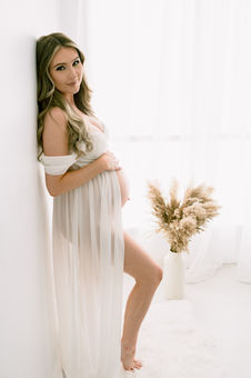 Mother to be in a white gown against wall during maternity session