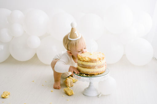 baby in party hat biting cake during first smash and splash session