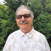 Jean-Jaqcues portrait in front of trees wearing tinted glasses and smiling