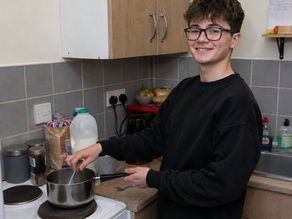 Young person preparing a meal independently in Oasis Care supported accommodation with staff support nearby.
