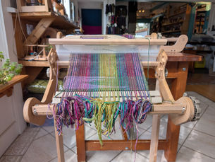 Rigid heddle loom with green and purple warp/weft. A handwoven scarf in progress.