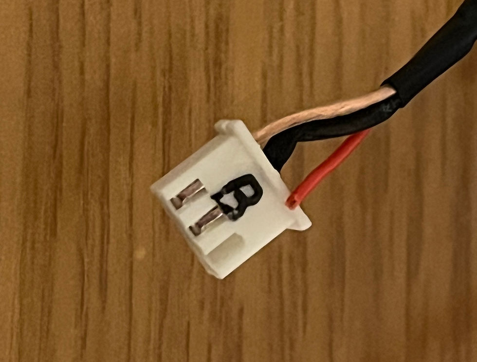 White plastic connector with "B" printed, attached to black and red wires. Set against a wooden surface background.