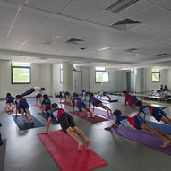 Yoga instructor leading large group of pre-teen students in plank pose on colorful mats in mirrored school studio — East West Yoga Singapore ages 9 to 12