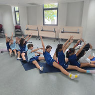 Pre-teen girls doing seated twist stretch together on yoga mats in school — East West Yoga Singapore ages 9 to 12