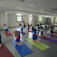 Yoga instructor leading large group of pre-teen students in seated side stretch pose on colorful mats — East West Yoga Singapore school ages 9 to 12