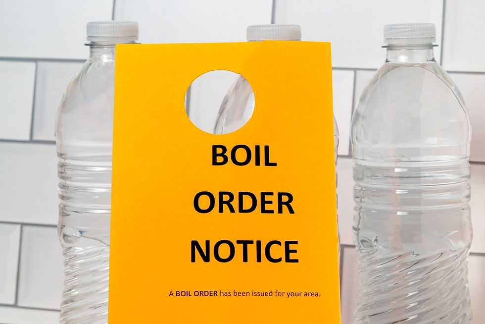 Yellow Boil Order Notice sign between clear water bottles against a white tiled wall.