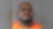Mugshot of a serious-faced man in an orange prison jumpsuit against a plain gray background.