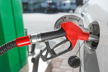 Red fuel nozzle pumping gas into a white car at a station, with a green pump and bright daylight in the background