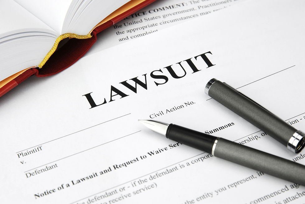 Lawsuit form on desk with two pens and an open book; bold LAWSUIT title and legal text suggest a serious legal scene.