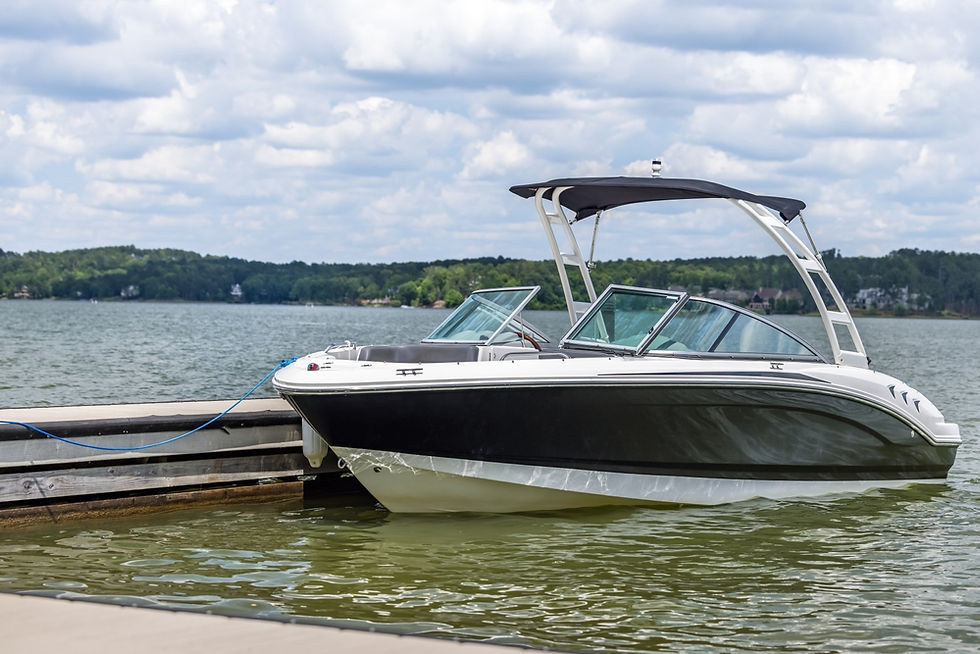 Black-and-white motorboat tied to a dock on a lake under cloudy skies, calm waters and wooded shoreline in the background.