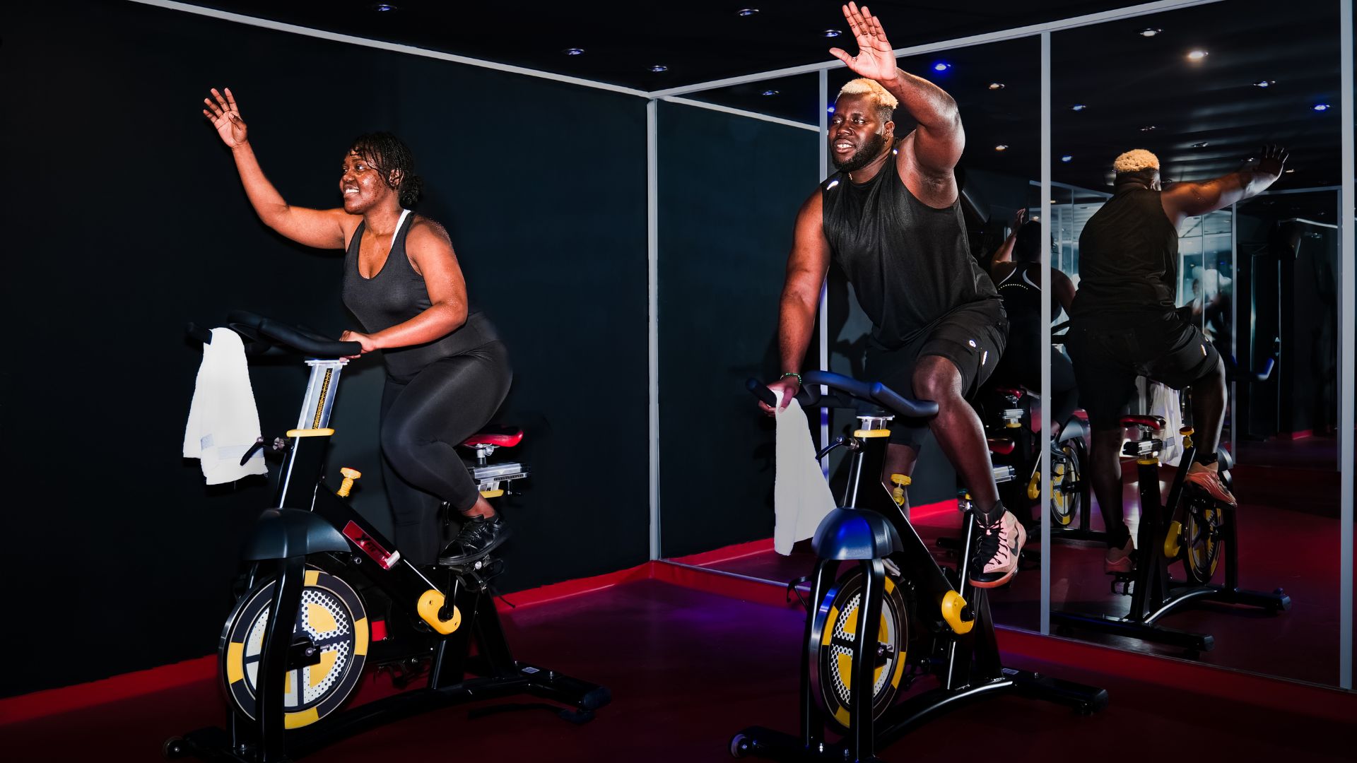 Two individuals enjoying a workout on stationary bikes. Experience the joy of exercise with diverse representation. Join the fitness journey and discover the benefits of indoor cycling for a healthier lifestyle.