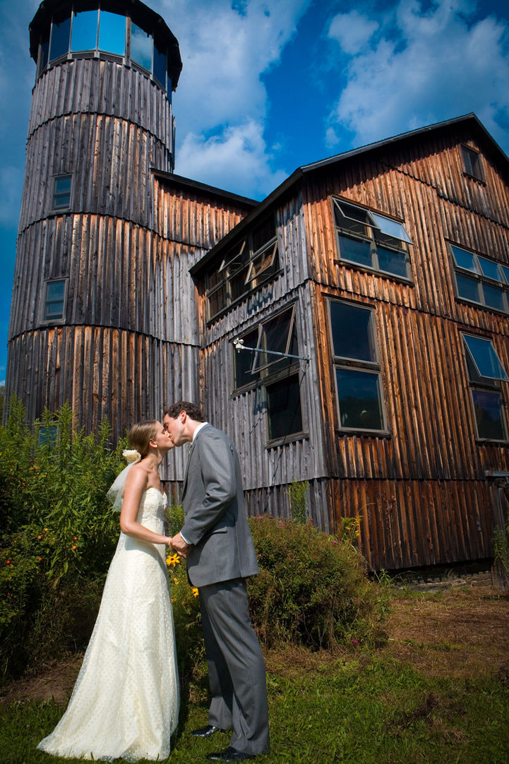 Bride and groom embrace in front of stunning wooden home with unique architectural structure 