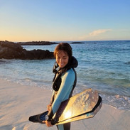 Woman holding long fins in a custom freediving wetsuit on a beach in Hawaii