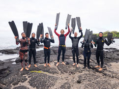 a group of freedivers gathers on the rocks with fins held in the air