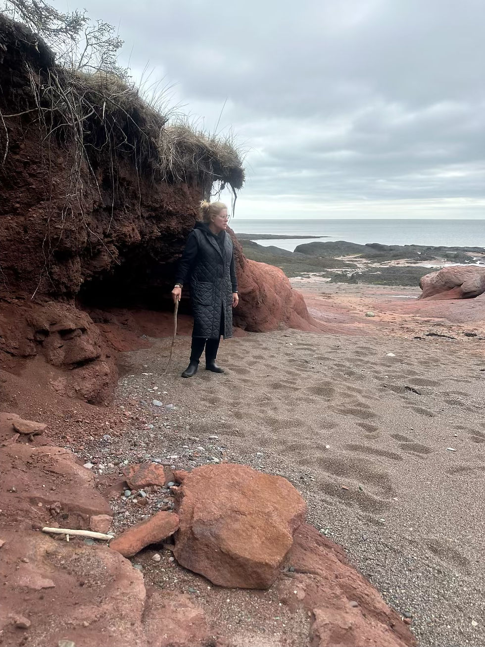 a woman, kimberley peacock, stands next to a red rock sea cave