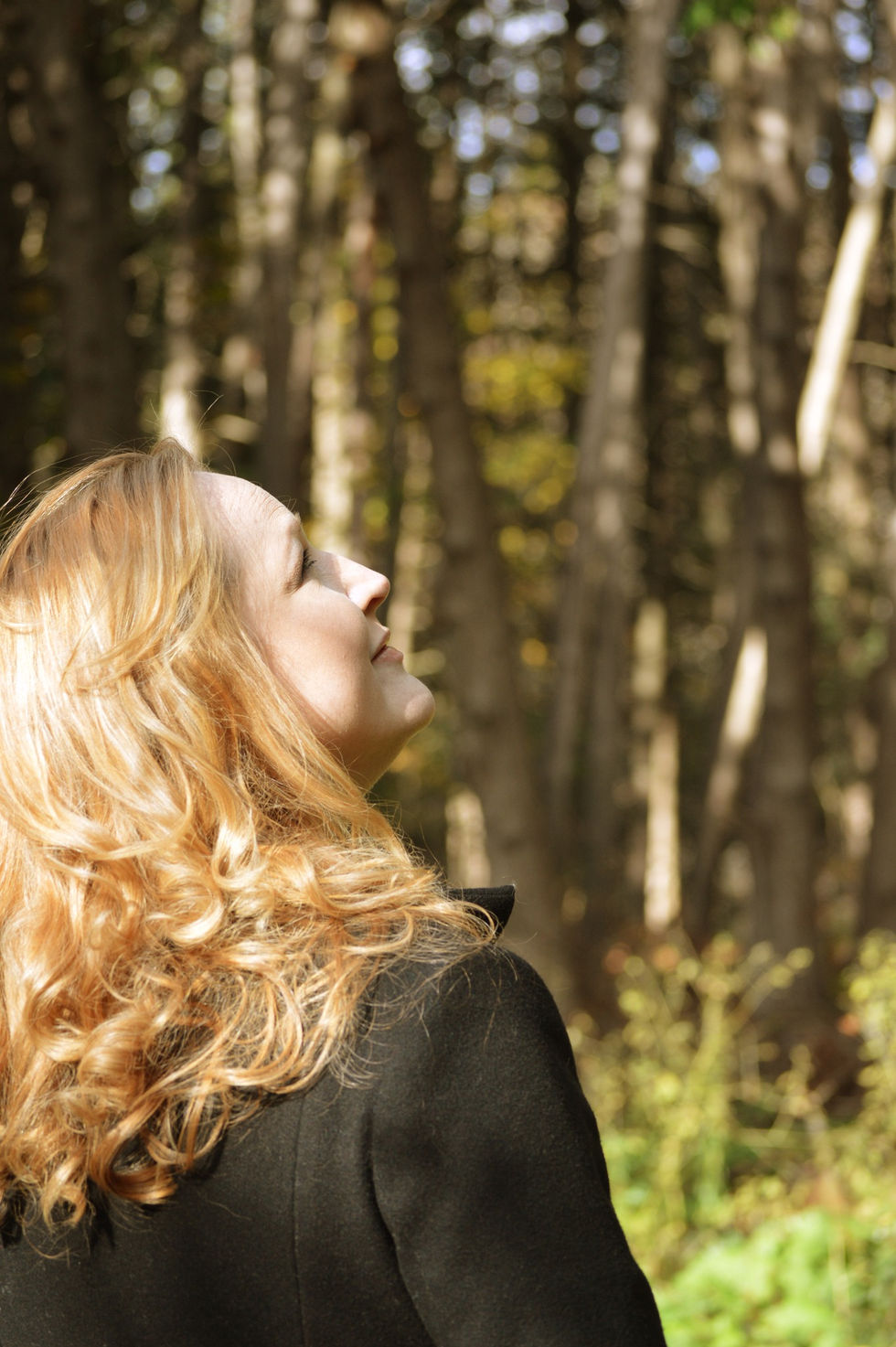 a woman in a black coat looks up at the trees