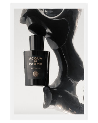 Fotografia creativa di una bottiglia di profumo Acqua di Parma Zafferano con riflesso scultoreo lucido su sfondo chiaro, realizzata da fotografo professionista di prodotti di lusso.