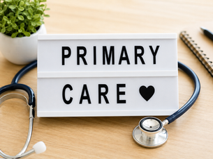 Lightbox on desk reads PRIMARY CARE with a heart, surrounded by a stethoscope, plant, notebook, and pen.