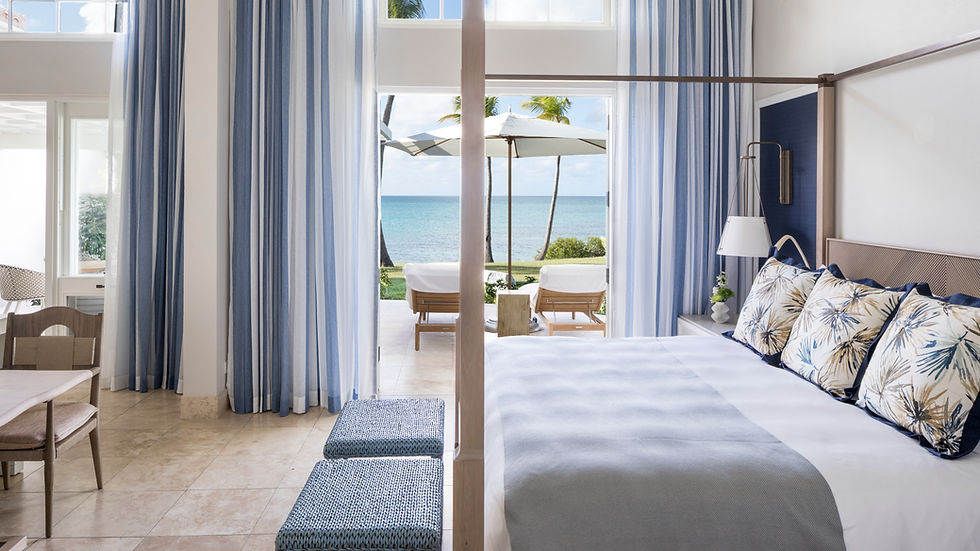 Elegant bedroom with blue and white decor, ocean view through large windows, striped curtains, palm trees, and patio seating outside. Calm mood.
