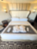 Luxurious hotel room with beige headboard, two robes, slippers on bed labeled "AZAMARA," patterned carpet, elegant lighting.