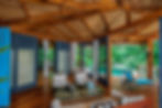 Tropical room with blue doors, wooden beams, and poolside deck. Cushioned chairs, glass table, and lush greenery create a relaxing vibe.