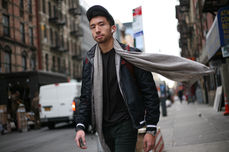 Street photography image of man in city wearing a baseball cap and scarf blowing in wind while looking at the camera.