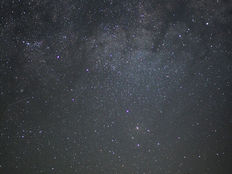 Silhouette of a person with a flashlight under a starry sky and Milky Way. Dark hill in the foreground, creating a serene, cosmic scene.
