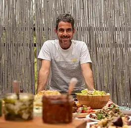 אושרי מחייך ליד שולחן עם אוכל ורקע במבוק.