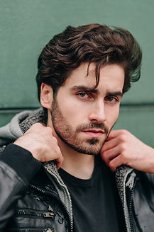 Schauspieler Timo Aust mit ernstem Blick in Lederjacke vor einem grünem Hintergrund