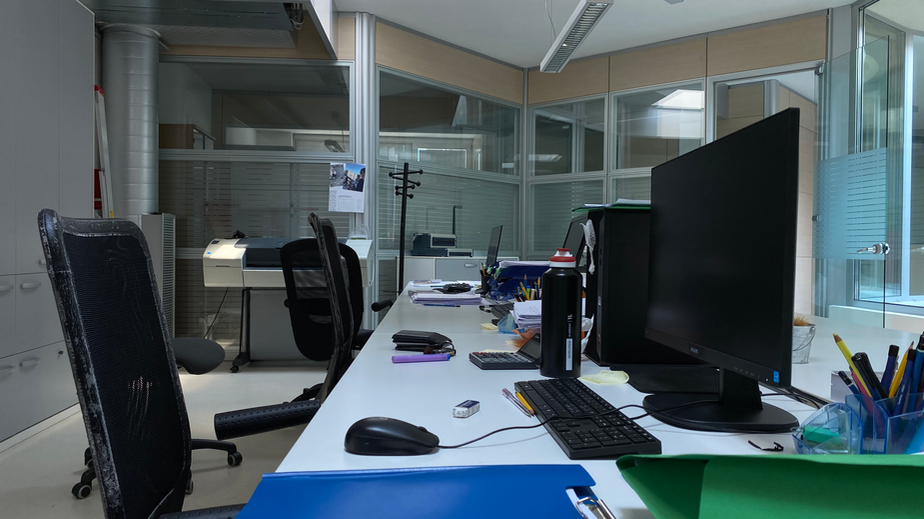dettaglio scrivania bianca con tre postazioni lavorative con computer neri e sedute nere