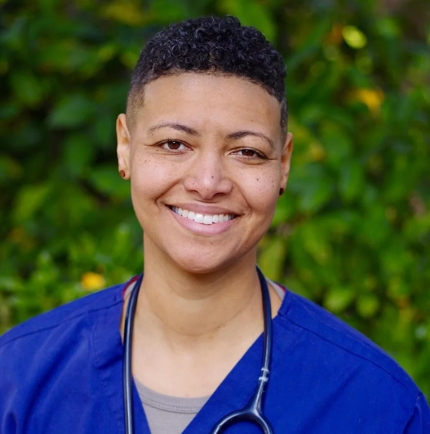 A portrait of Jennifer smiling, wearing blue scrubs with a stethoscope around her neck